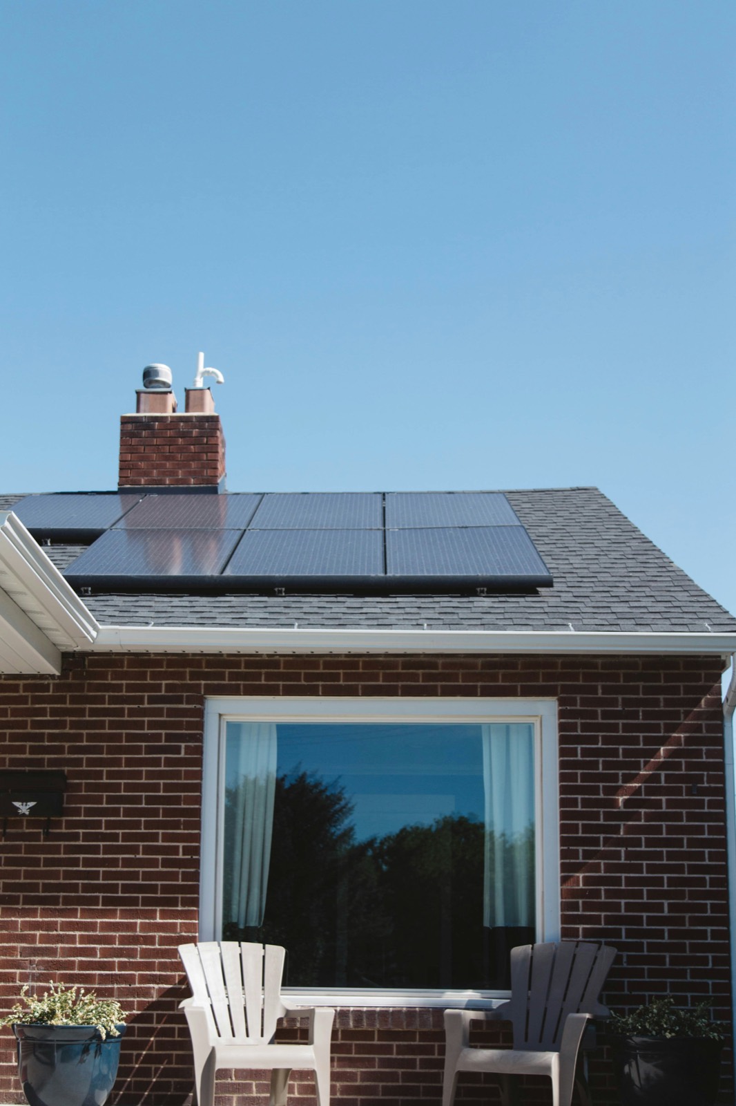 Brick house with black solar panels on the roof above a large living room window
