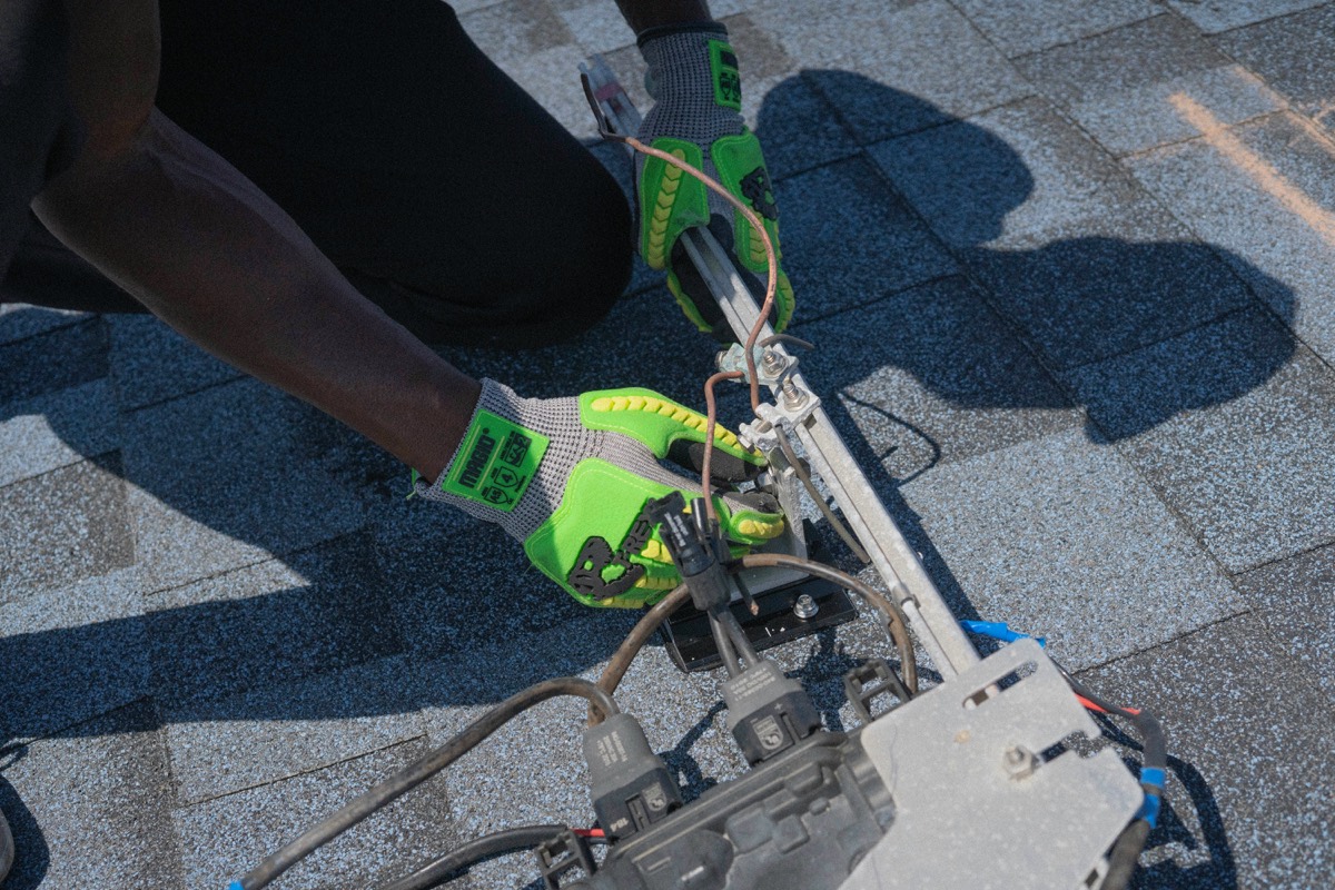 Gloved hands wiring a solar microinverter on a mounting rail, close-up